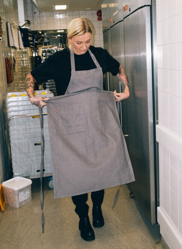 Kvinna i oversize t-shirt knyter sitt linneförkläde bakom restaurangens kök.