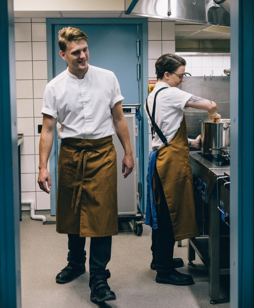 Kockar i restaurangkök bär förkläden och vita kockskjortor.