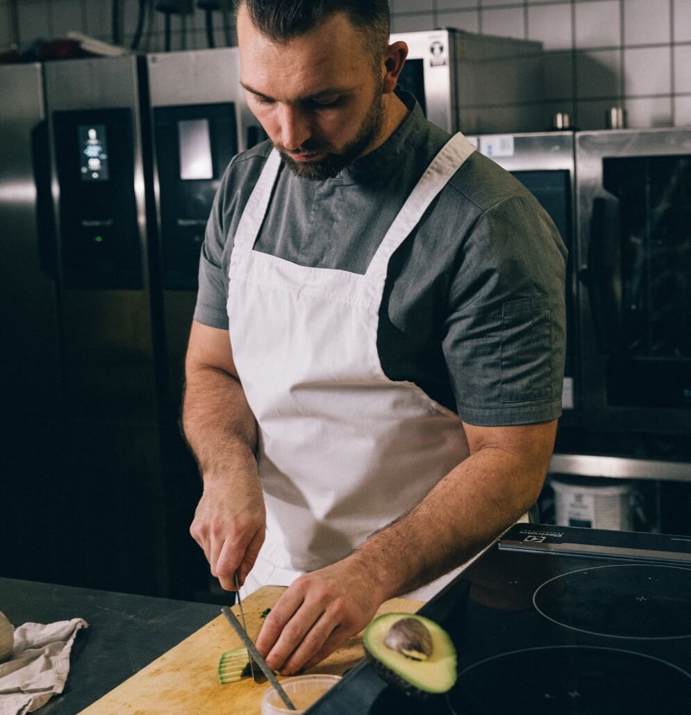 Kock förbereder mat i restaurangkök med vitt förkläde.